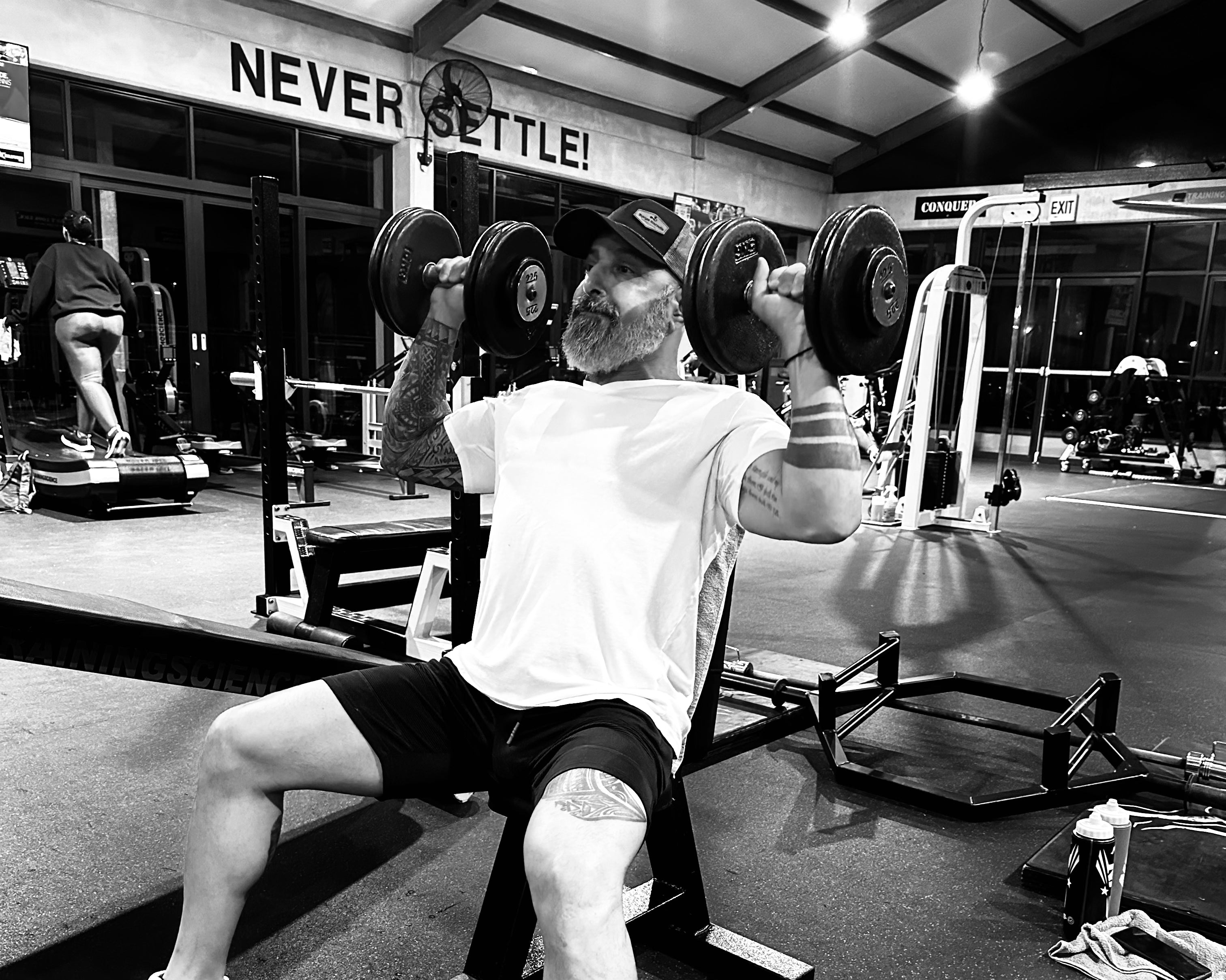Person lifting weights in a gym with 'Never Settle' sign in the background