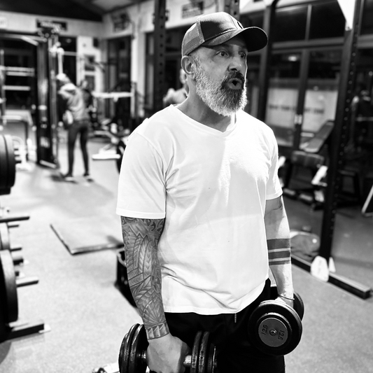 Man in a gym holding dumbbells with equipment and people in the background
